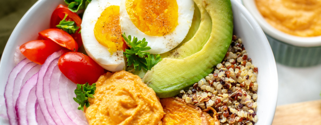  A bowl filled with Quinia, Avocado, Onions, Sweet Potatoes, Cherry Tomatoes and Egg.